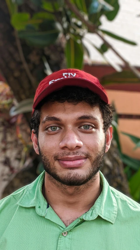 a man wearing a green shirt and a red hat, by Ahmed Yacoubi, with palm trees in the back, wearing a backwards baseball cap, friendly face, student