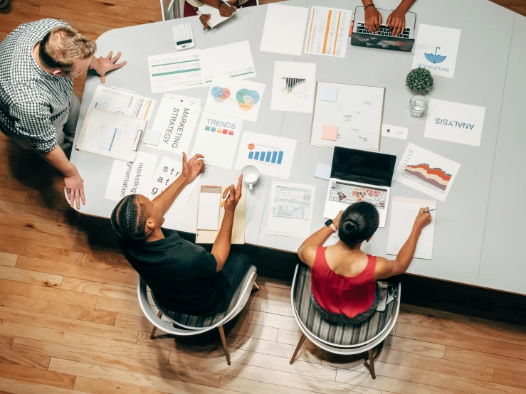 a group of people sitting around a table with papers, by Emma Andijewska, pexels contest winner, product design, 9 9 designs, wide high angle view, bold graphics