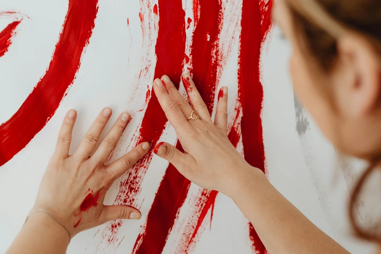 a woman painting on a wall with red paint, a painting, by Julia Pishtar, pexels contest winner, action painting, hands pressed together in bow, red and white stripes, woman holding another woman, on a white table