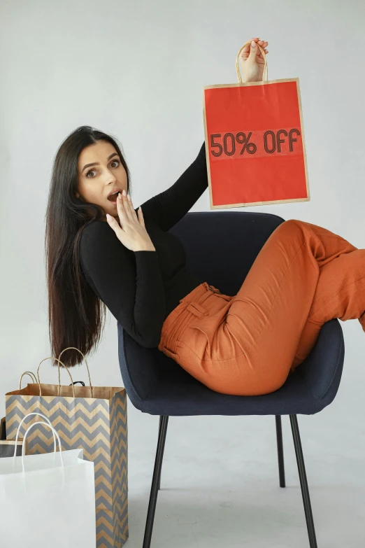 a woman sitting on a chair holding a sign that says 50 % off, pexels contest winner, wearing pants, shocked look, black and terracotta, malls