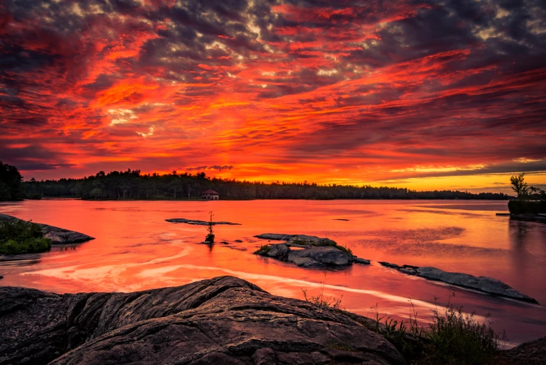 a sunset over a body of water with rocks in the foreground, by Jesper Knudsen, pexels contest winner, fiery red, swedish countryside, panoramic shot, fan favorite