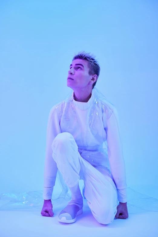 a woman sitting on the ground in a white outfit, an album cover, inspired by Russell Dongjun Lu, an epic non - binary model, brightly lit blue room, looking to his side, (snow)