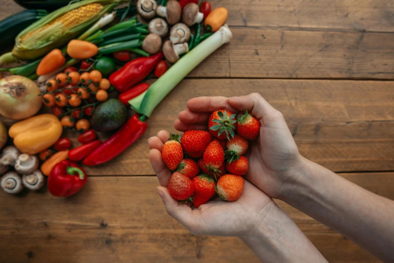 a person holding a bunch of strawberries in their hands, by Juan O'Gorman, pexels contest winner, confident holding vegetables, on wooden table, avatar image, multicoloured