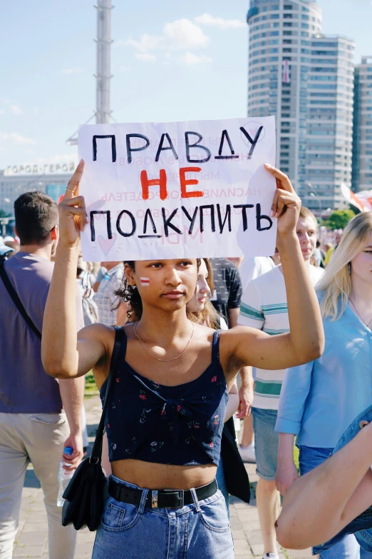 a woman holding a sign in front of a crowd of people, by Attila Meszlenyi, tumblr, russia in 2 0 2 1, square, diverse, 🚿🗝📝