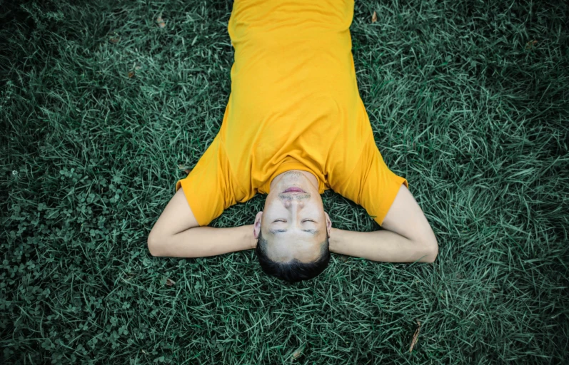 a man laying on top of a lush green field, inspired by Ren Hang, pexels contest winner, realism, wearing a modern yellow tshirt, avatar image, buddhist monk, an asian woman