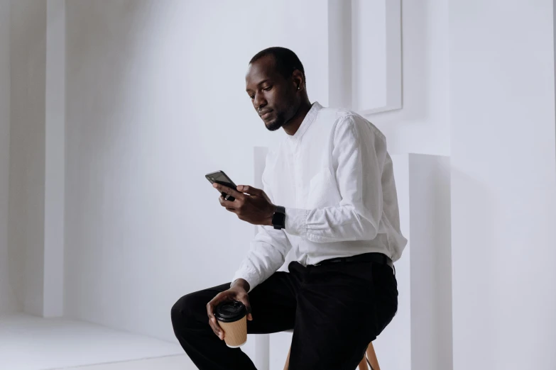 a man sitting on a chair using a cell phone, trending on pexels, minimalism, ( ( dark skin ) ), white dress shirt, avatar image, morning coffee