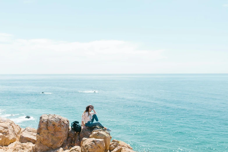 a woman sitting on top of a rock next to the ocean, profile image