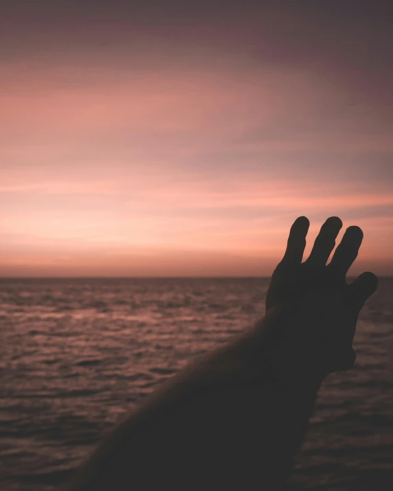 a person holding their hand up in front of the ocean, in a sunset haze, lgbtq, instagram photo, dark. no text