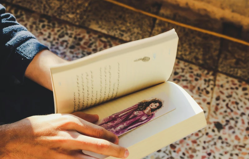 a close up of a person holding a book, a portrait, pexels contest winner, magic realism, lying down, an olive skinned, story book design, casually dressed