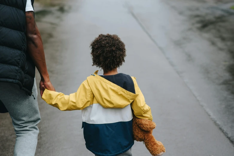 a man and a child walking down a street holding hands, by Arabella Rankin, pexels contest winner, yellow raincoat, holding a teddy bear, mixed race, on a gray background