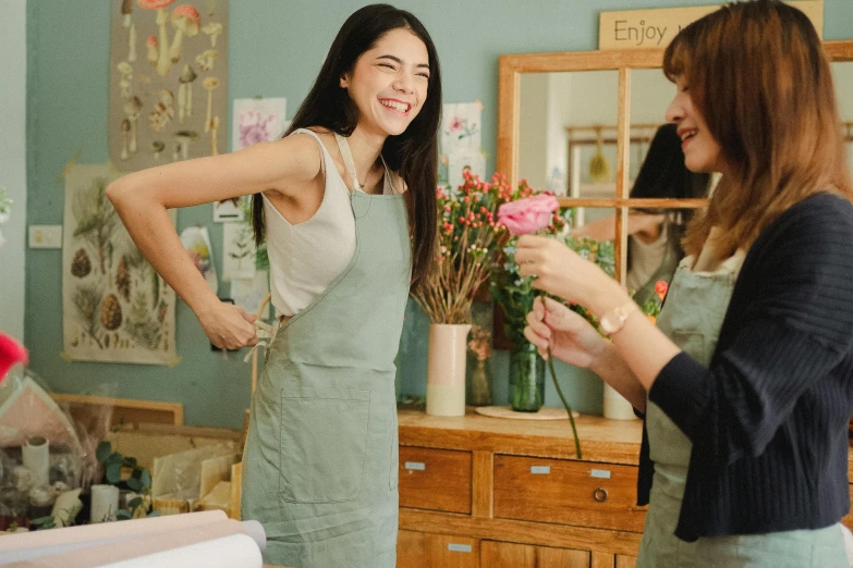 a woman standing next to another woman in a room, inspired by Ruth Jên, pexels contest winner, flower shop scene, being delighted and cheerful, wearing an apron, dua lipa
