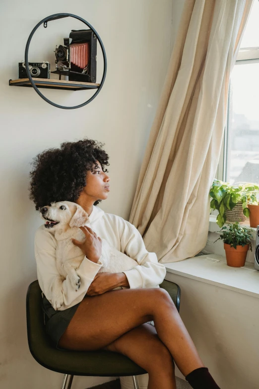 a woman sitting on a chair holding a dog, trending on pexels, window sill with plants, with afro, comfy, 1 4 8 0 s