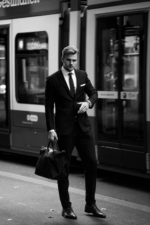 a man in a suit standing in front of a train, a black and white photo, inspired by Adrian Zingg, tumblr, very attractive and beautiful, business men, man walking through city, one man is blond