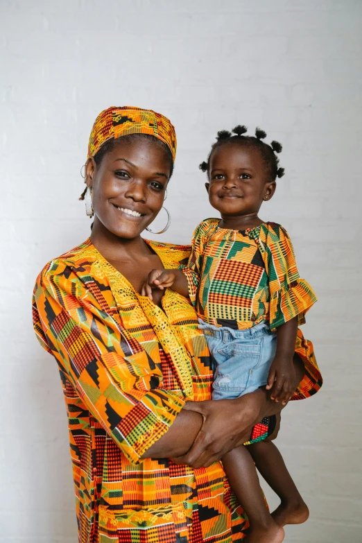 a woman holding a child in her arms, pexels contest winner, afrofuturism, wearing an african dress, both smiling for the camera, mango, uk