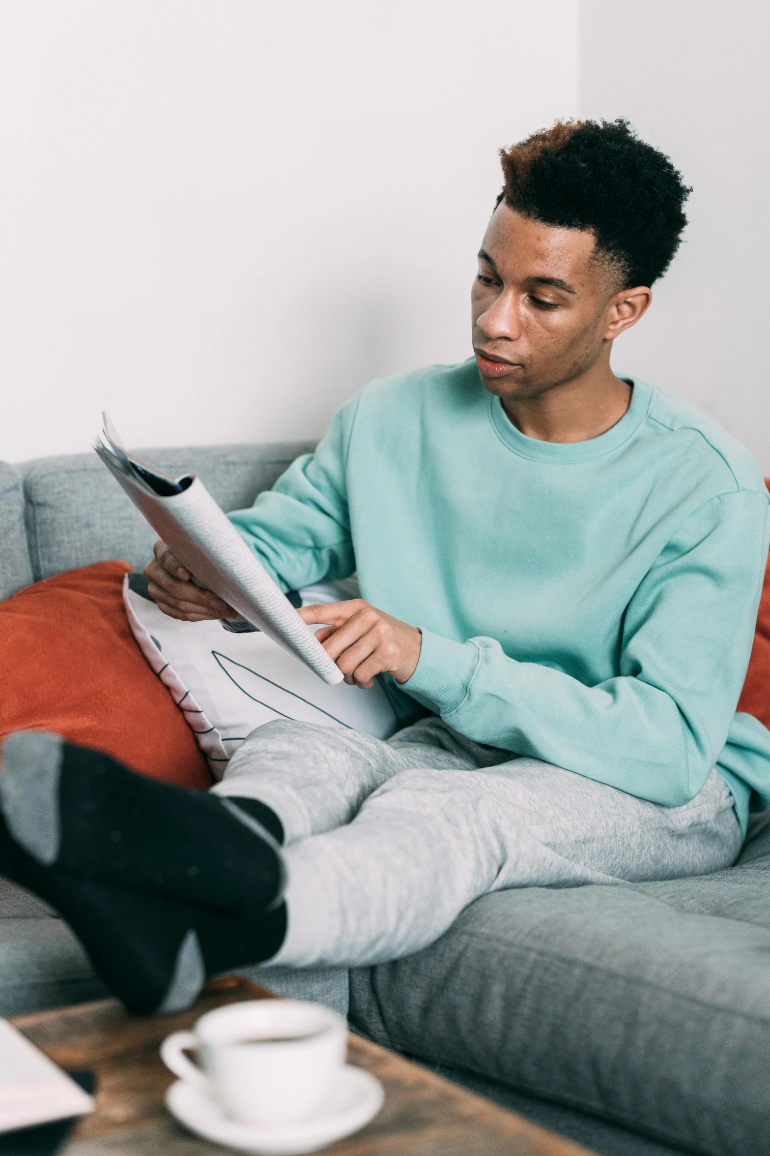 a man sitting on a couch reading a magazine, by Cosmo Alexander, trending on pexels, black teenage boy, with teal clothes, 15081959 21121991 01012000 4k, casually dressed