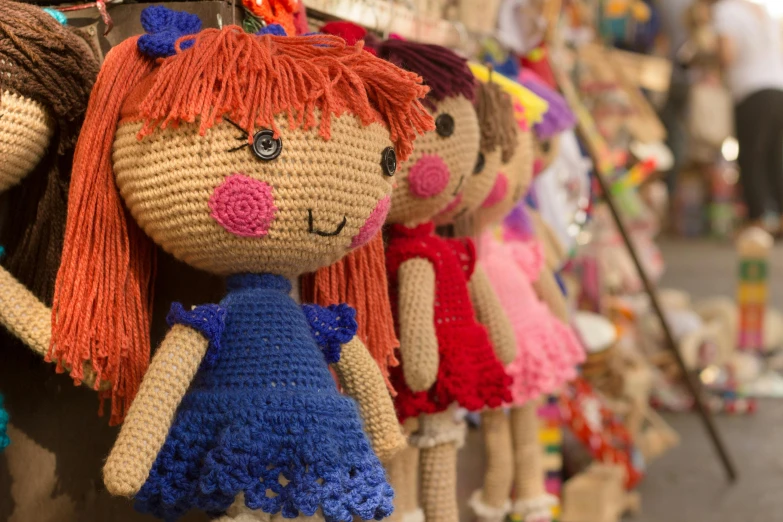 a group of crocheted dolls hanging on a wall, a cartoon, by Lee Loughridge, pexels, colored market stand, cute girl, in a mall, gorgeous features