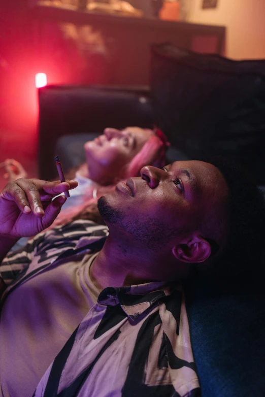 a couple of men laying on top of a couch, inspired by Nan Goldin, trending on pexels, mangeta smoke red light, purple scene lighting, black man, in a cinema