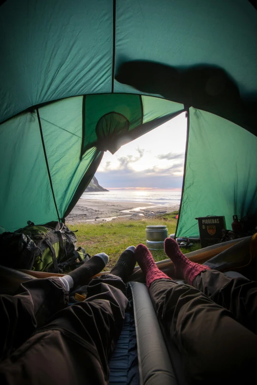 a couple of people laying inside of a tent, hills and ocean, adventuring, overlooking the ocean, meadows