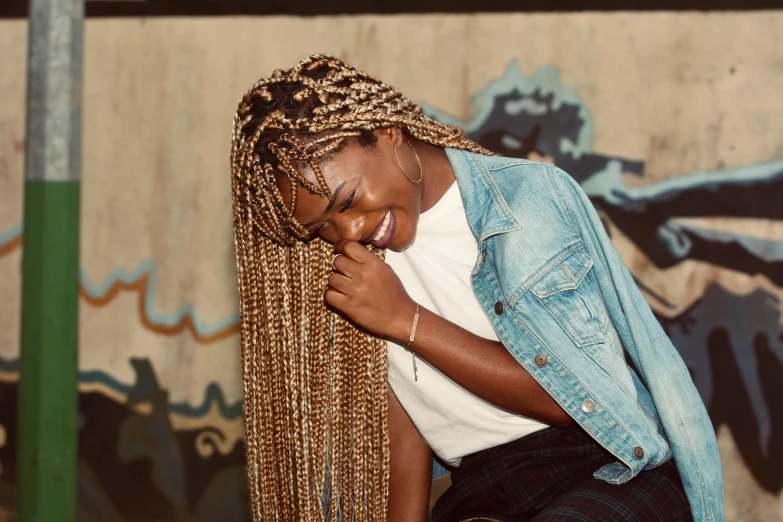 a woman sitting on a skateboard in front of a graffiti wall, an album cover, trending on pexels, hyperrealism, cornrows braids, smiling laughing, relaxed. gold background, long braided silver hair
