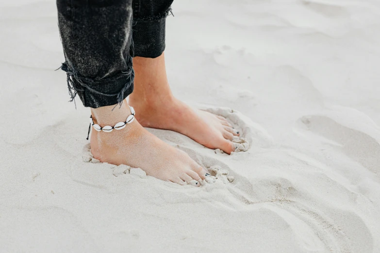a person standing on top of a sandy beach, by Nina Hamnett, trending on pexels, white and silver, handcrafted, glossy white metal, feet