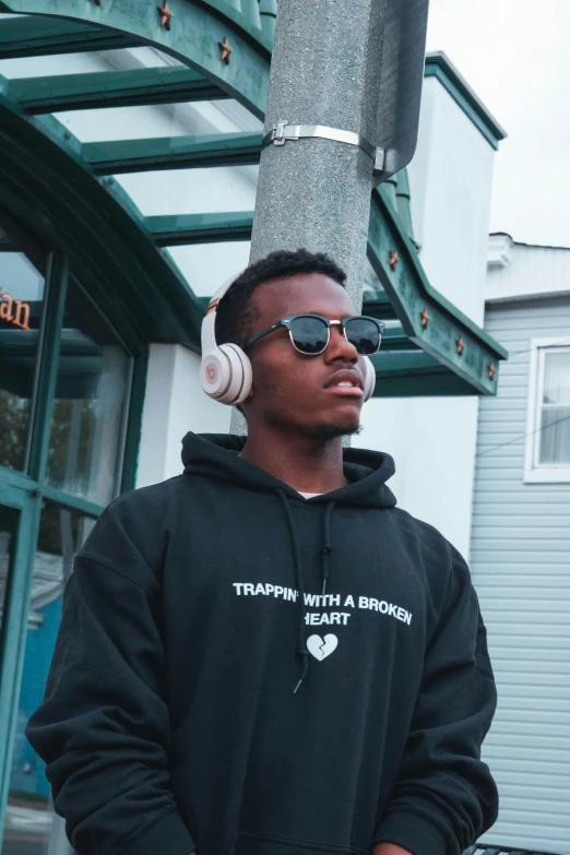 a man wearing headphones standing in front of a building, trending on unsplash, ( brown skin ), trap, official store photo, wholesome