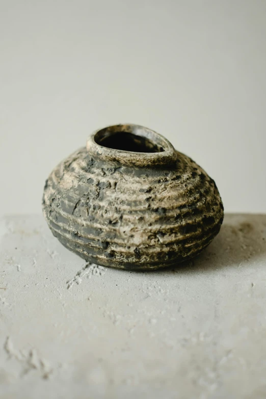 a close up of a small vase on a table, inspired by Hendrik Gerritsz Pot, unsplash, mingei, brownish old fossil remnant, made of tar, terraced, medium wide front shot