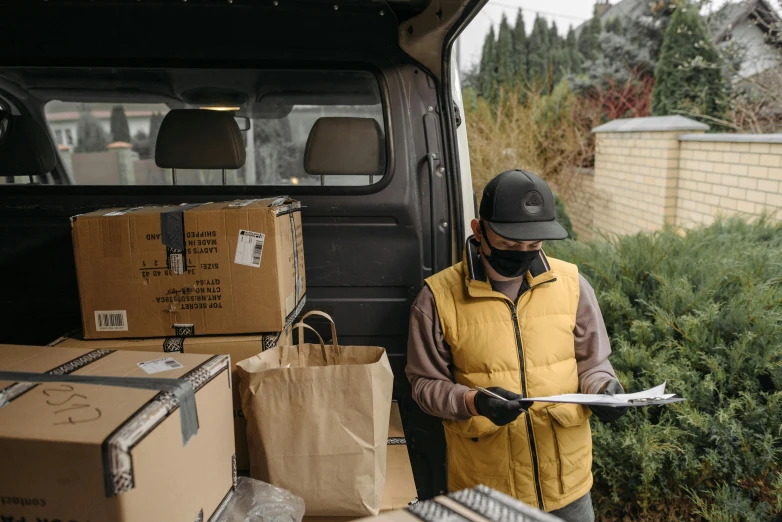 a man standing next to a van filled with boxes, by Carey Morris, pexels contest winner, holding a clipboard, covid, highly detaild, brown