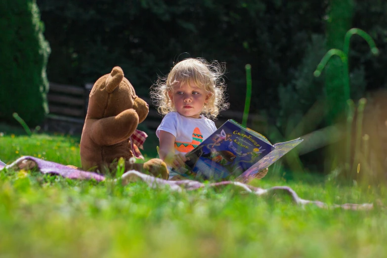 a little girl that is sitting in the grass with a teddy bear, inspired by William Stott, pexels contest winner, reading in library, in the sun, colour photograph, flashing lights