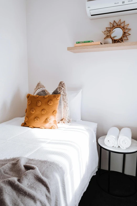 a white bed sitting in a bedroom next to a wall mounted air conditioner, by Nicolette Macnamara, trending on unsplash, some sandy yellow pillows, white background, boy's room, earthy colours