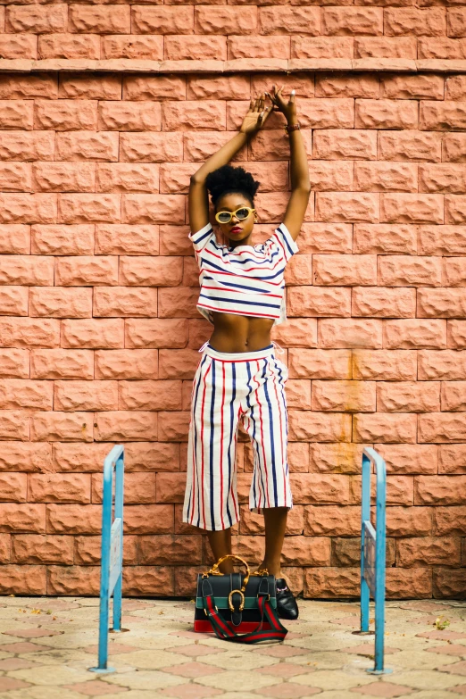 a woman standing in front of a brick wall, by Lily Delissa Joseph, pexels contest winner, stripey pants, croptop and shorts, colored photo, african woman