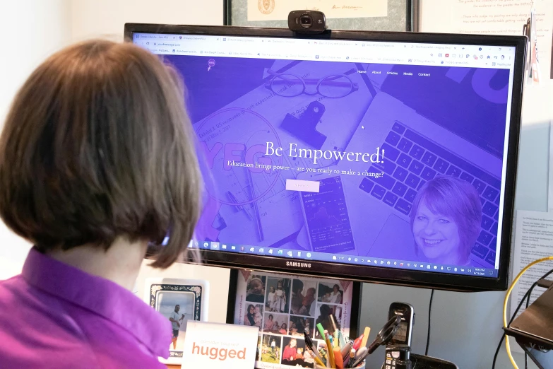 a woman sitting at a desk in front of a computer, inspired by Ella Guru, happening, close up to the screen, website, purple themed, photographed from behind