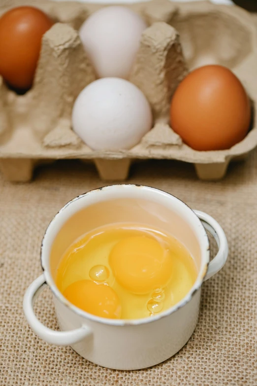 a white bowl filled with eggs next to a carton of eggs, a portrait, trending on pexels, renaissance, cups and balls, local foods, half image