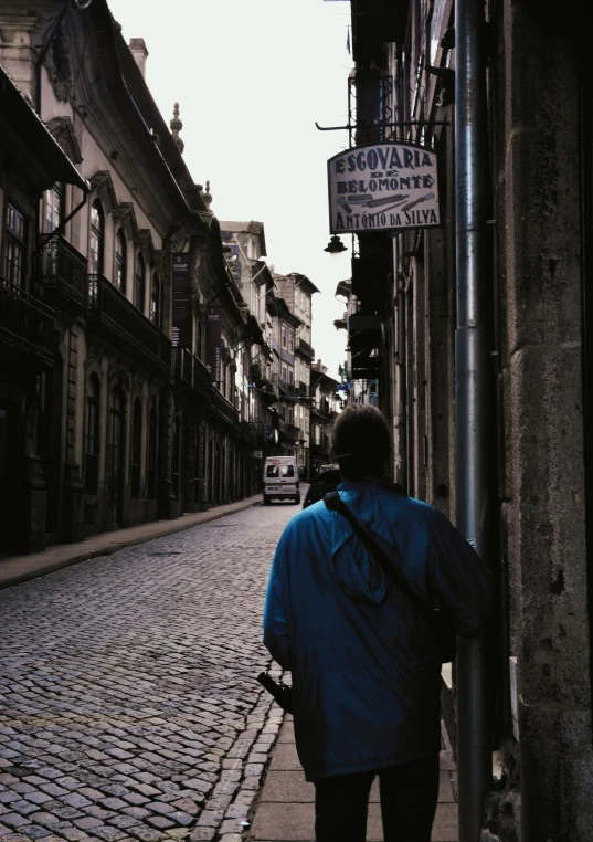 a person walking down a cobblestone street, an album cover, inspired by Oswaldo Viteri, pexels contest winner, renaissance, streets of salvador, facing away from camera, blue, university