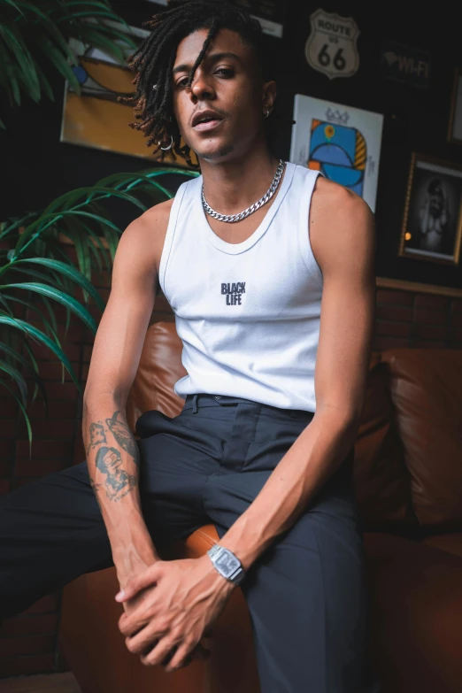 a man sitting on top of a brown couch, an album cover, inspired by Clifford Ellis, trending on pexels, white tank top, rapper jewelry, playboi carti portrait, tight black tanktop