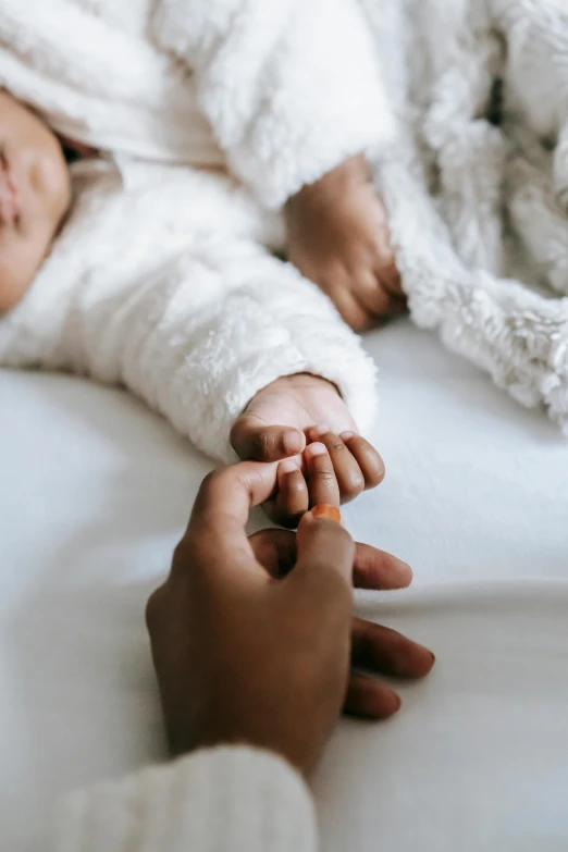 a close up of a person holding a baby's hand, unsplash, visual art, laying on a bed, varying ethnicities, elegantly dressed, ignant