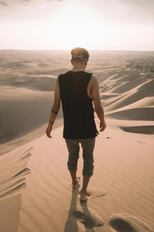 a man walking on a sand dune in the desert, an album cover, trending on pexels, wearing a tanktop, blonde guy, lost in thought, peru