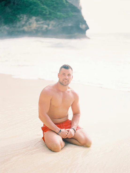 a man sitting on a beach next to the ocean, beefcake pose, bali, profile image, sunfaded