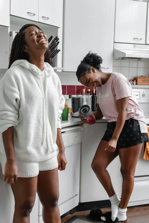 a couple of women standing next to each other in a kitchen, trending on unsplash, happening, bra and shorts streetwear, both laughing, wearing white pajamas, black young woman