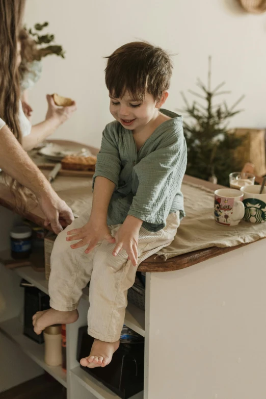 a little boy sitting on top of a counter next to a woman, by Elizabeth Durack, pexels contest winner, baggy pants, earthy, small kitchen, festive atmosphere