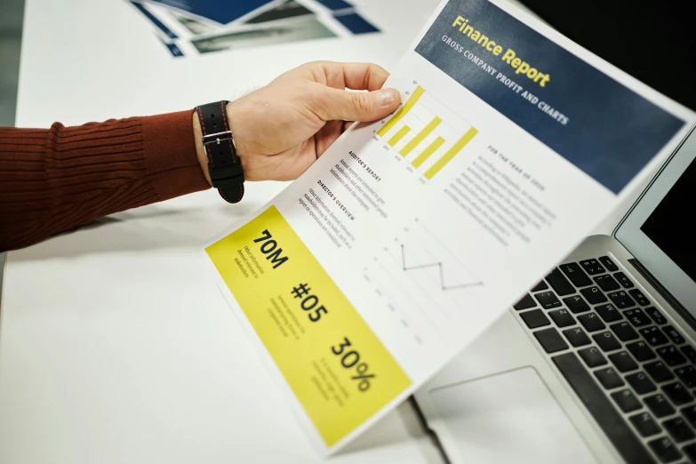 a person holding a piece of paper in front of a laptop, a poster, pexels, analytical art, stats, yellow and black color scheme, selling insurance, printed page