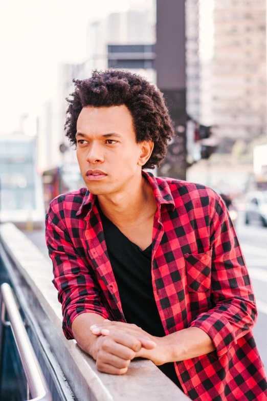 a man in a red and black shirt leaning on a railing, an album cover, by Jacob Toorenvliet, long afro hair, actor, sydney park, mid length portrait photograph