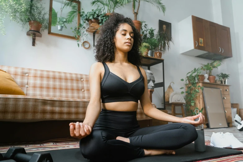 a woman sitting on a yoga mat in a living room, trending on pexels, indian girl with brown skin, wearing black tight clothing, paradise garden massage, avatar image