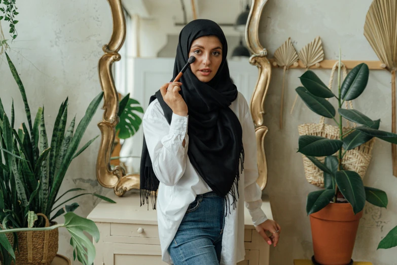 a woman standing in front of a mirror talking on a cell phone, a charcoal drawing, trending on pexels, hurufiyya, wearing fluffy black scarf, photoshoot for skincare brand, middle eastern style vendors, covered in plants