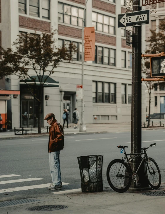 a man standing on the side of a road next to a street sign, trending on unsplash, standing in a city center, low quality photo, sitting alone, standing on street corner