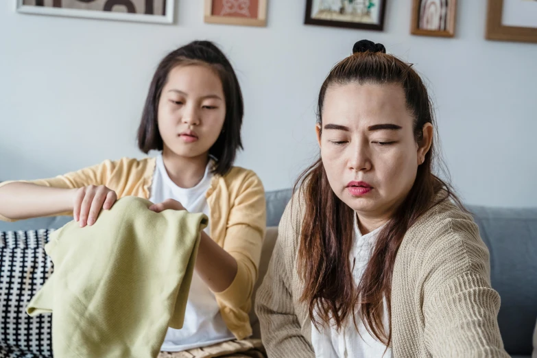 a couple of women sitting on top of a couch, a picture, trending on pexels, mingei, damaged japanese clothes, sweating profusely, family friendly, with yellow cloths