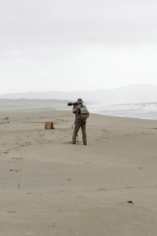 a man standing on top of a sandy beach, sniper, slight overcast weather, photographs, south african coast