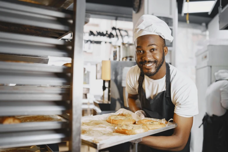 a man holding a tray of bread in a kitchen, pexels contest winner, african canadian, server in the middle, cute bakery shop, avatar image