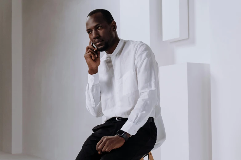 a man sitting on a chair talking on a cell phone, inspired by Theo Constanté, trending on pexels, renaissance, white dress shirt, man is with black skin, standing elegantly, black on white