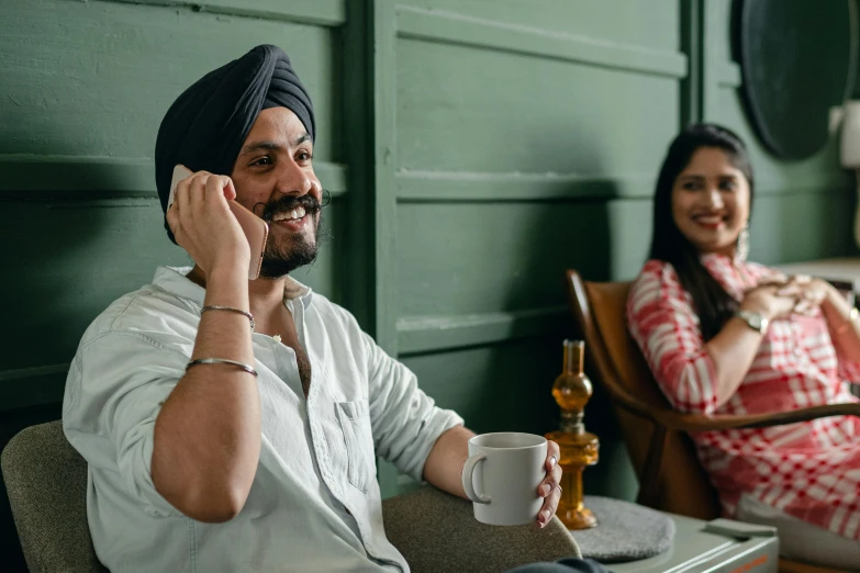 a man in a turban talking on a cell phone, inspired by Manjit Bawa, pexels contest winner, smiling couple, next to a cup, customers, sitting across the room