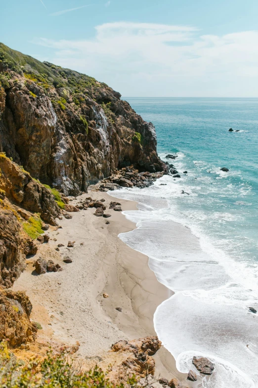 a sandy beach next to the ocean on a sunny day, malibu canyon, looking down a cliff, lush surroundings, wellington